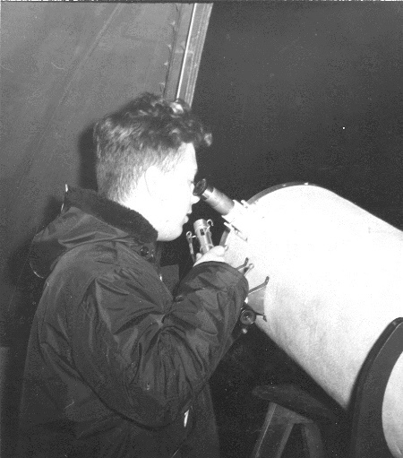 Charles, wearing a winter coat is looking through the Borror Observatory telescope eyepiece while speaking into a microphone on a winter night in 1963.