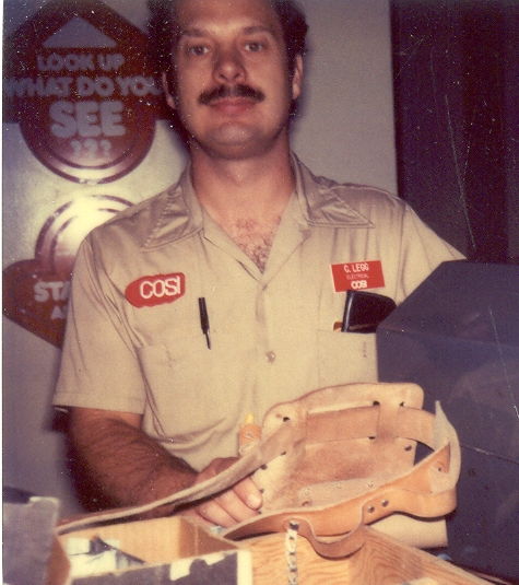 Charles is standing in front of the Center of Science and Industry glass elevator in 1980 wearing his tan colored C O S I work shirt and red name badge.