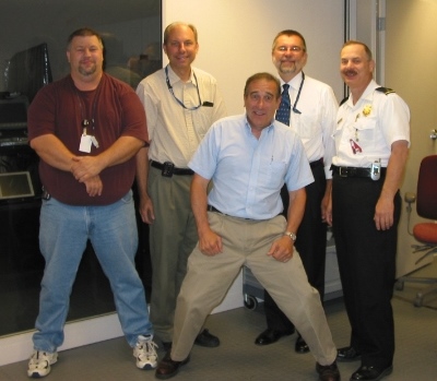 Group of civilian technology people posing with Lieutenant Charles Legg in 2002 outside the computer server room at the fire complex on Parsons Avenue.