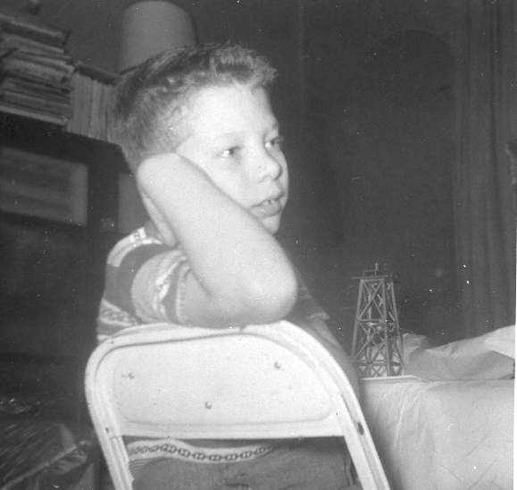 A 10 year old Charles is seated at a metal chair and is looking back over his arm while holding his head up with his hand. He has a day dreamer look about him.