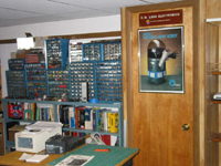 Shelves of book are seen with many small part drawers sitting on top that contain electronic parts. There is also a storage closet with a personal robot on the door.